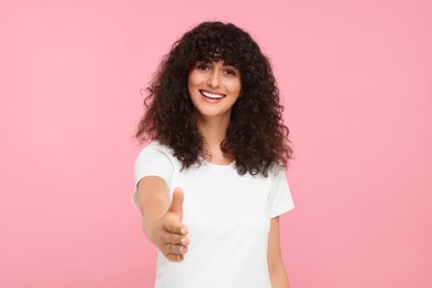 Photo of Happy young woman welcoming and offering handshake on pink background