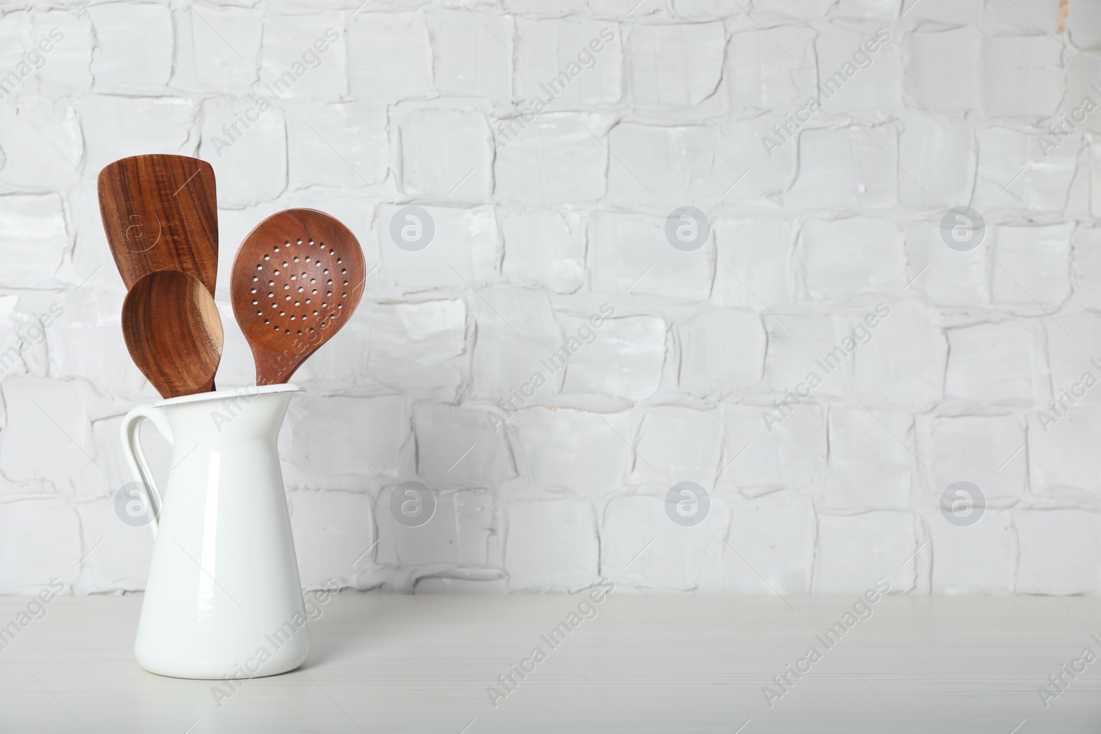 Photo of Set of wooden kitchen utensils in jug on table near white wall. Space for text