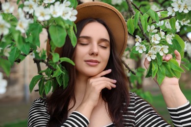 Beautiful woman in hat near blossoming tree on spring day