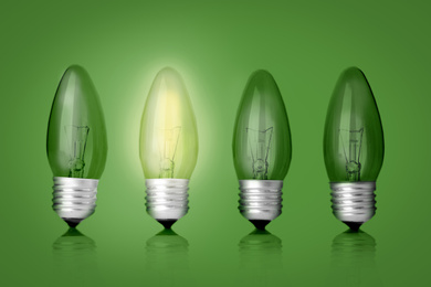 Image of Idea concept. Glowing light bulb among others on green background