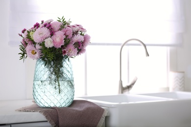 Vase with beautiful chrysanthemum flowers on countertop in kitchen, space for text. Interior design