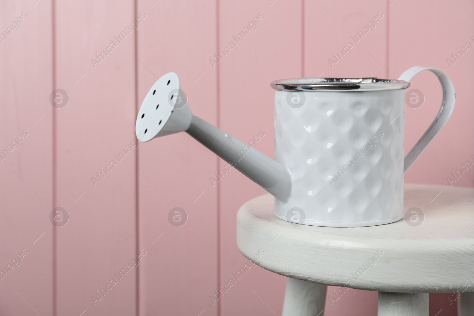 Photo of White metal watering can on table against pink wooden background