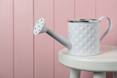 White metal watering can on table against pink wooden background