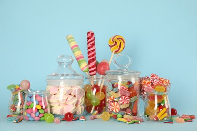 Jars with different delicious candies on light blue background