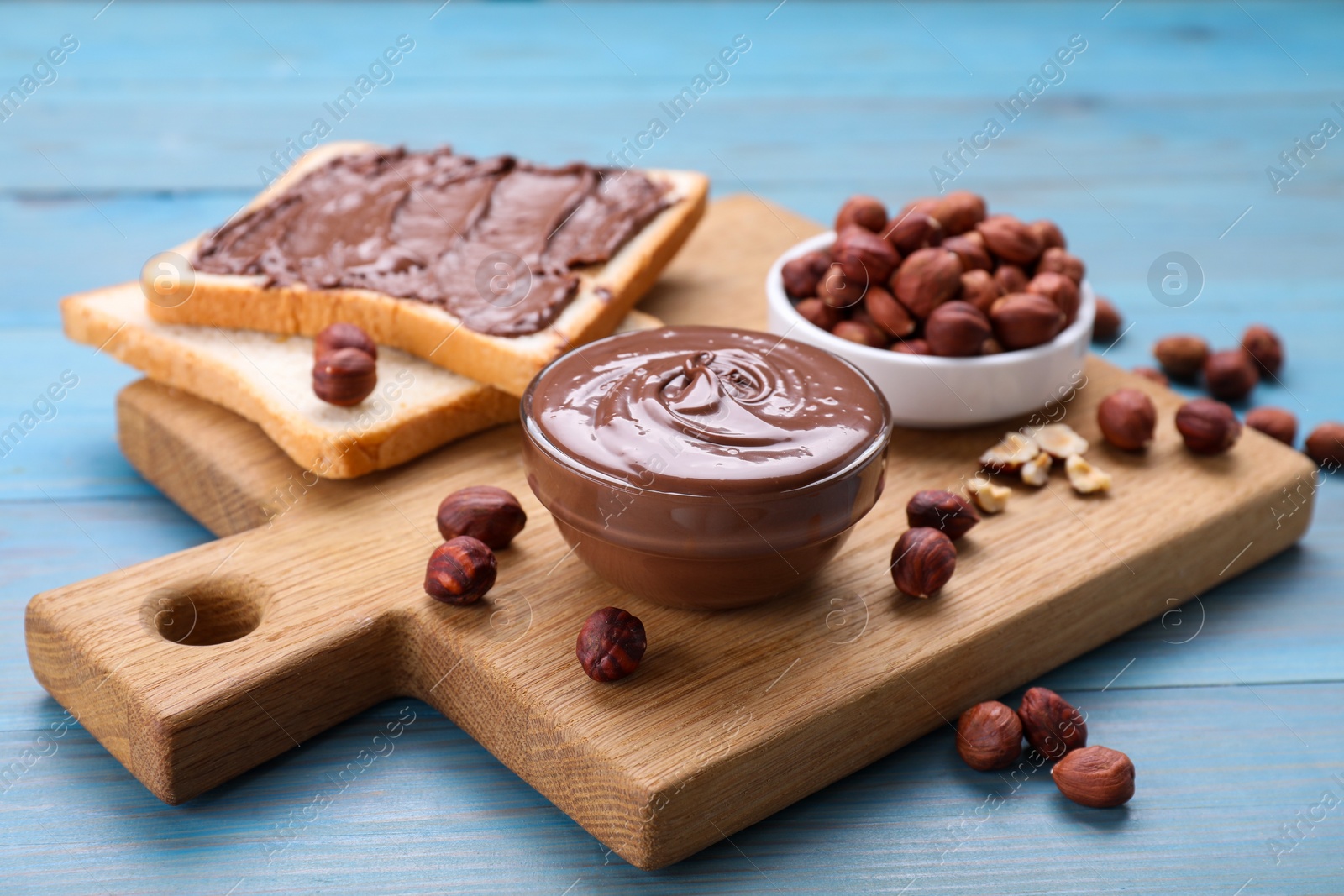 Photo of Toasts with tasty chocolate paste and nuts on light blue wooden table