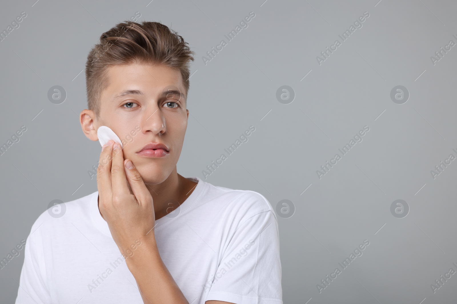 Photo of Handsome man cleaning face with cotton pad on grey background, space for text