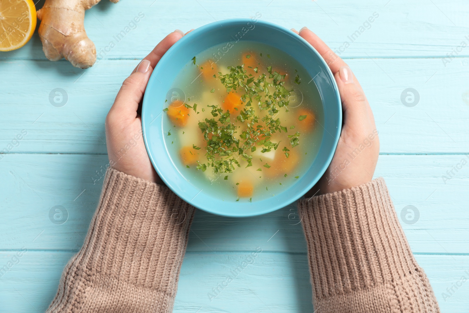 Photo of Sick woman holding bowl of fresh homemade soup to cure flu at table, top view
