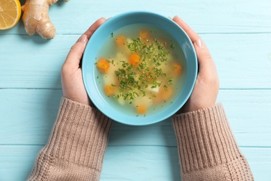 Photo of Sick woman holding bowl of fresh homemade soup to cure flu at table, top view