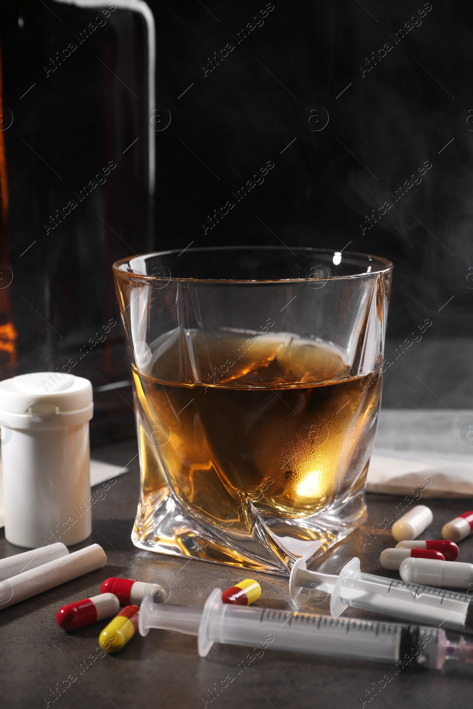 Photo of Alcohol and drug addiction. Whiskey in glass, syringes, pills and cigarettes on grey table