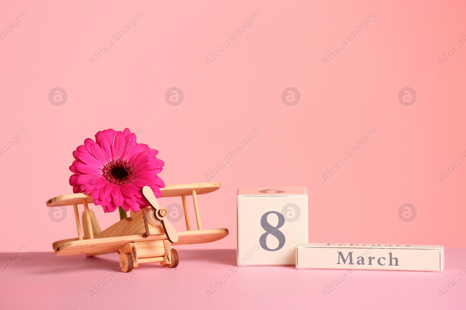 Photo of Composition with wooden plane and flower on table against color background, space for text. International Women's Day