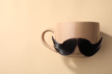 Artificial moustache and cup on beige background, top view. Space for text