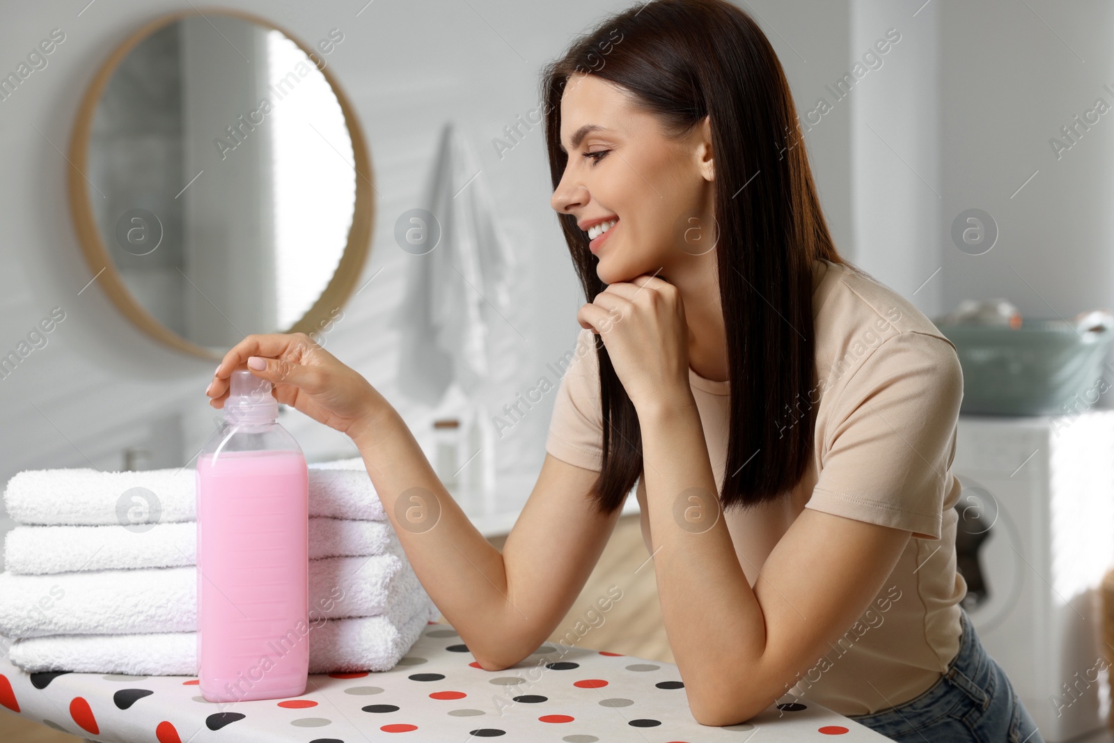 Photo of Woman near clean towels and fabric softener in bathroom