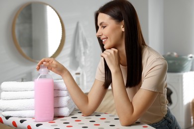 Photo of Woman near clean towels and fabric softener in bathroom