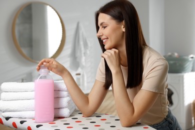 Woman near clean towels and fabric softener in bathroom