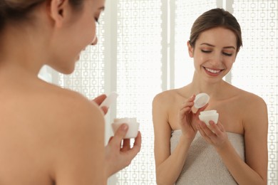 Photo of Young woman with face cream near mirror in bathroom