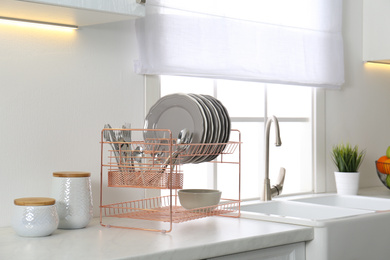 Photo of Clean dishes on drying rack in modern kitchen interior