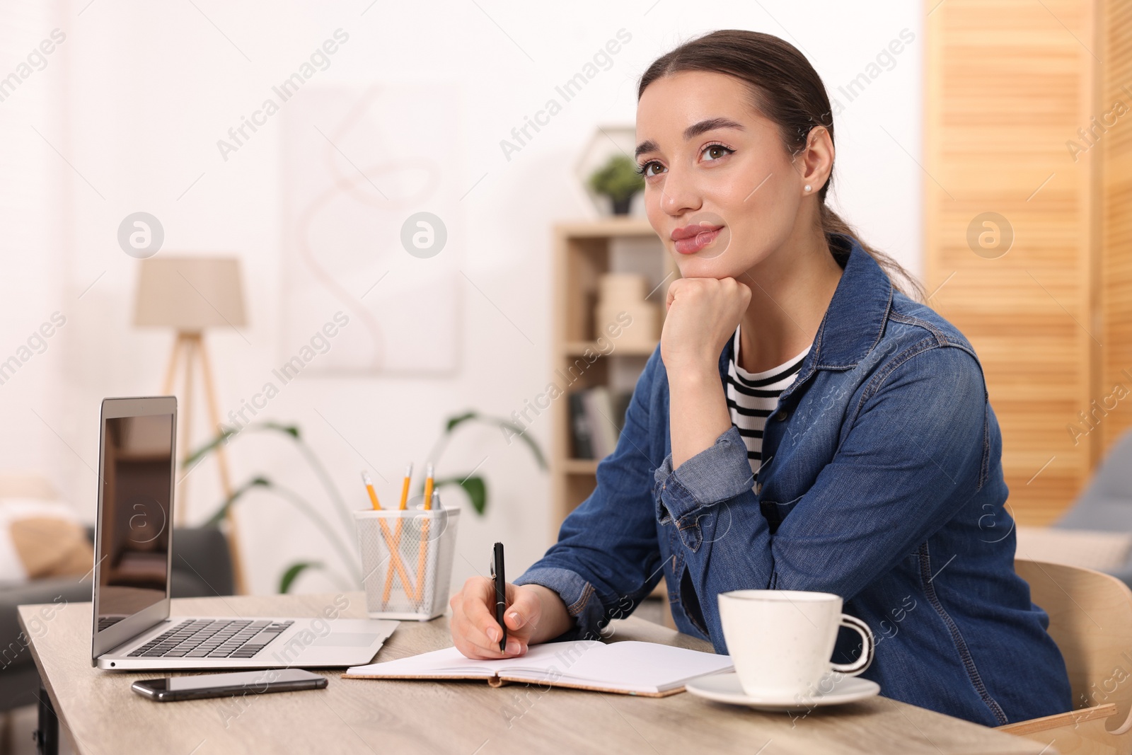 Photo of Young woman writing in notebook at wooden table indoors