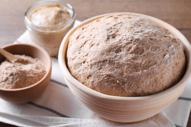 Photo of Fresh sourdough in proofing basket and flour on table, closeup