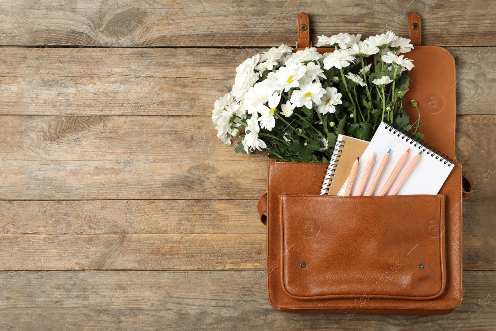 Photo of Leather briefcase with stationery and flowers on wooden table, top view with space for text. Teacher's Day