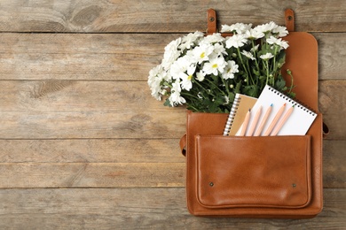 Leather briefcase with stationery and flowers on wooden table, top view with space for text. Teacher's Day