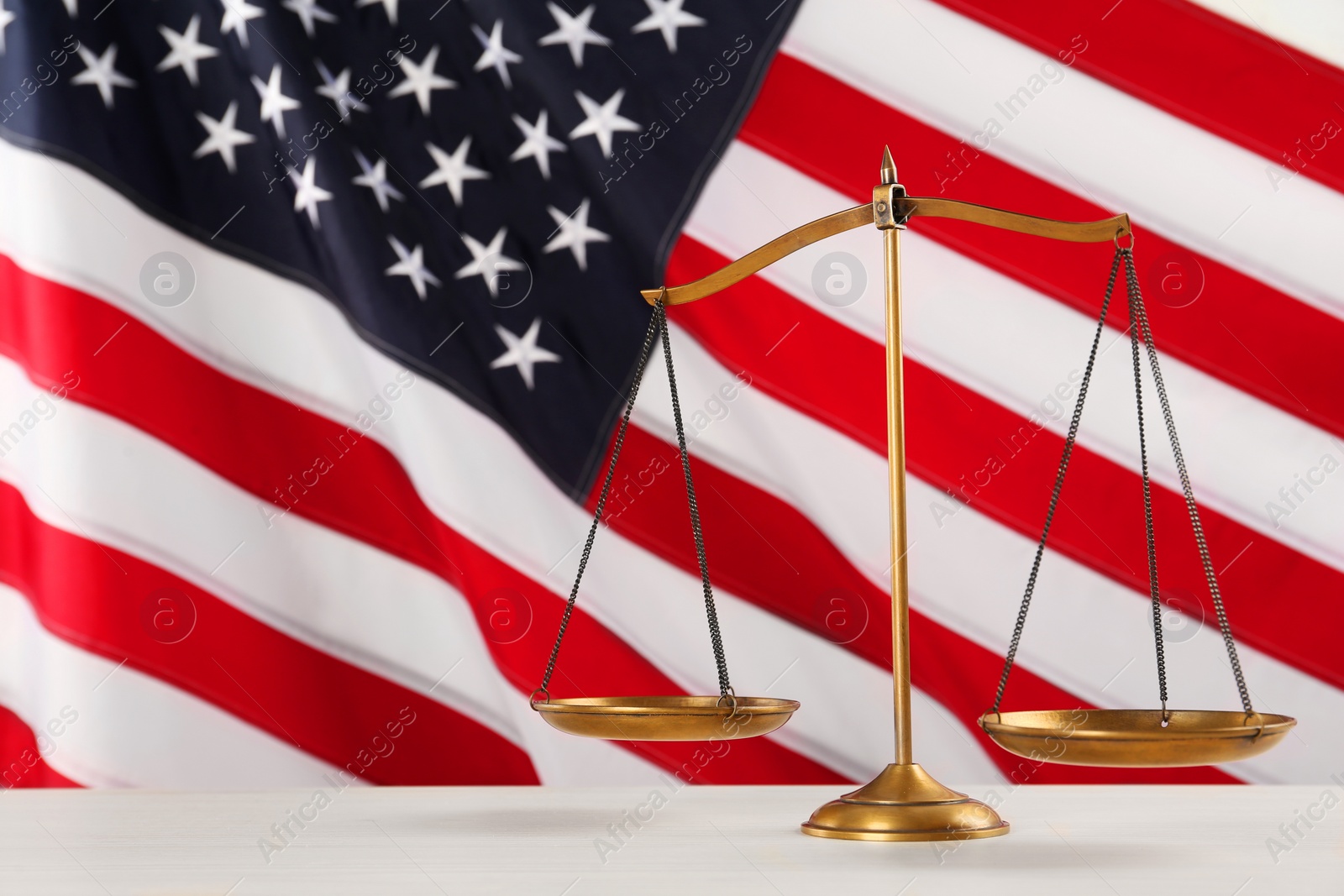 Photo of Scales of justice on white wooden table against American flag, space for text