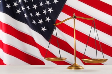 Photo of Scales of justice on white wooden table against American flag, space for text