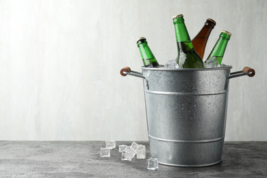 Metal bucket with beer and ice cubes on grey background. Space for text