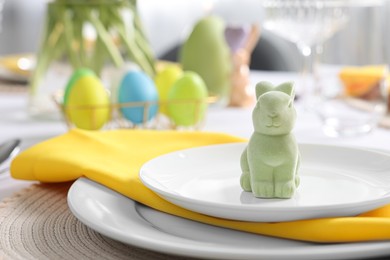 Photo of Festive table setting with cutlery, plate and bunny figure, closeup. Easter celebration