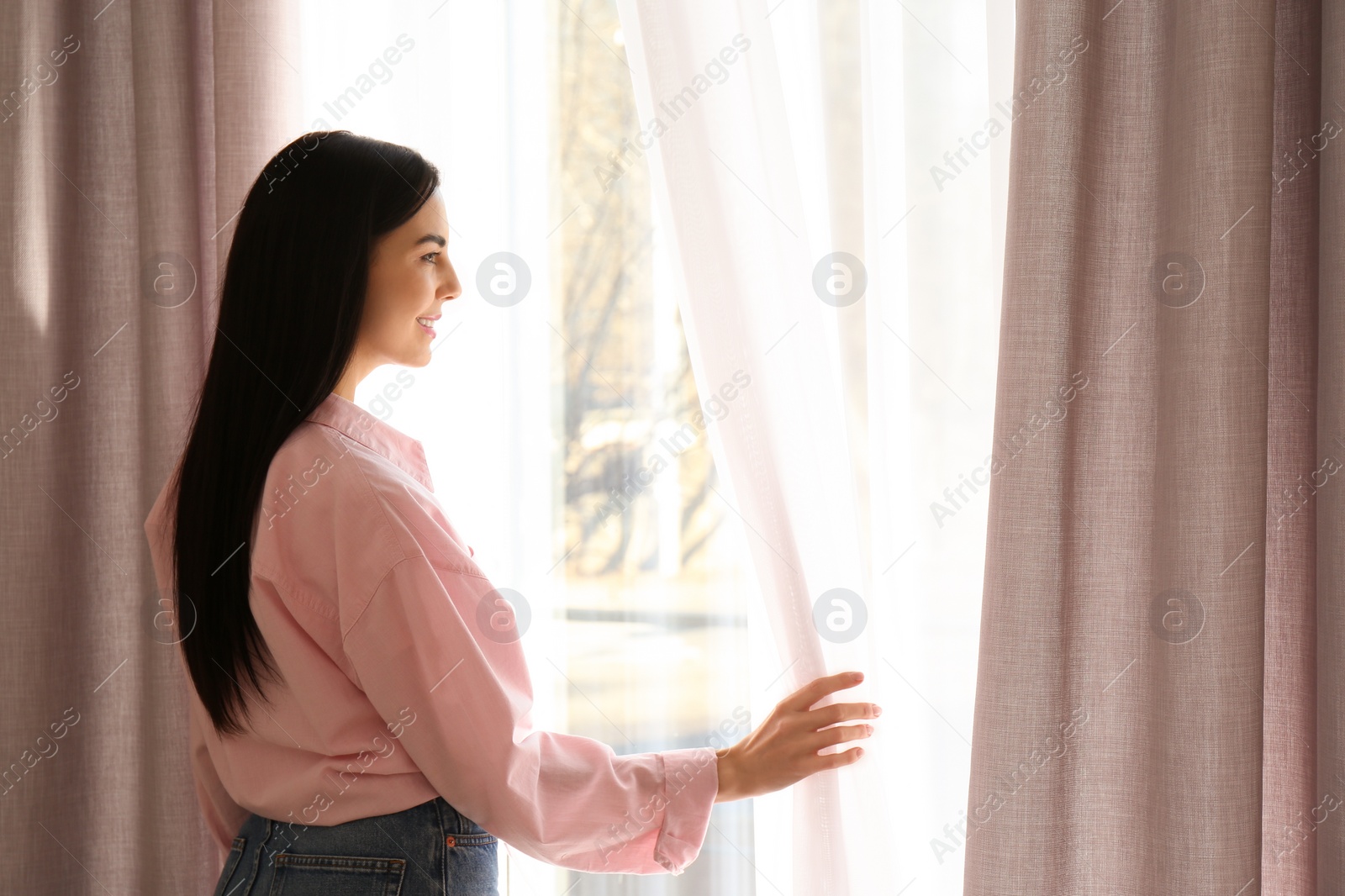 Photo of Woman opening window curtains at home in morning