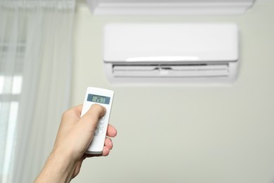 Photo of Man operating air conditioner with remote control indoors, closeup