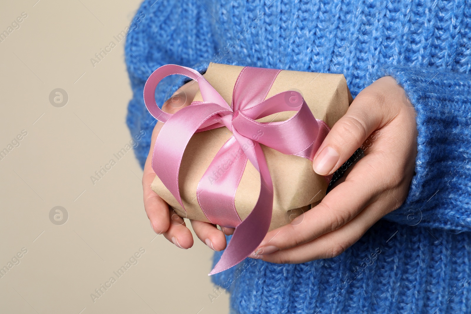 Photo of Woman holding gift box with pink bow on beige background, closeup. Space for text