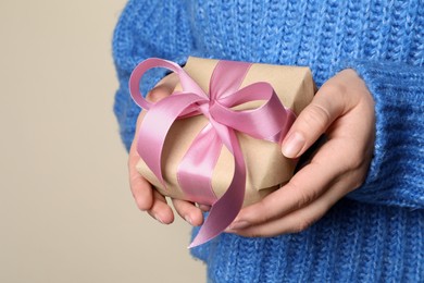Photo of Woman holding gift box with pink bow on beige background, closeup. Space for text