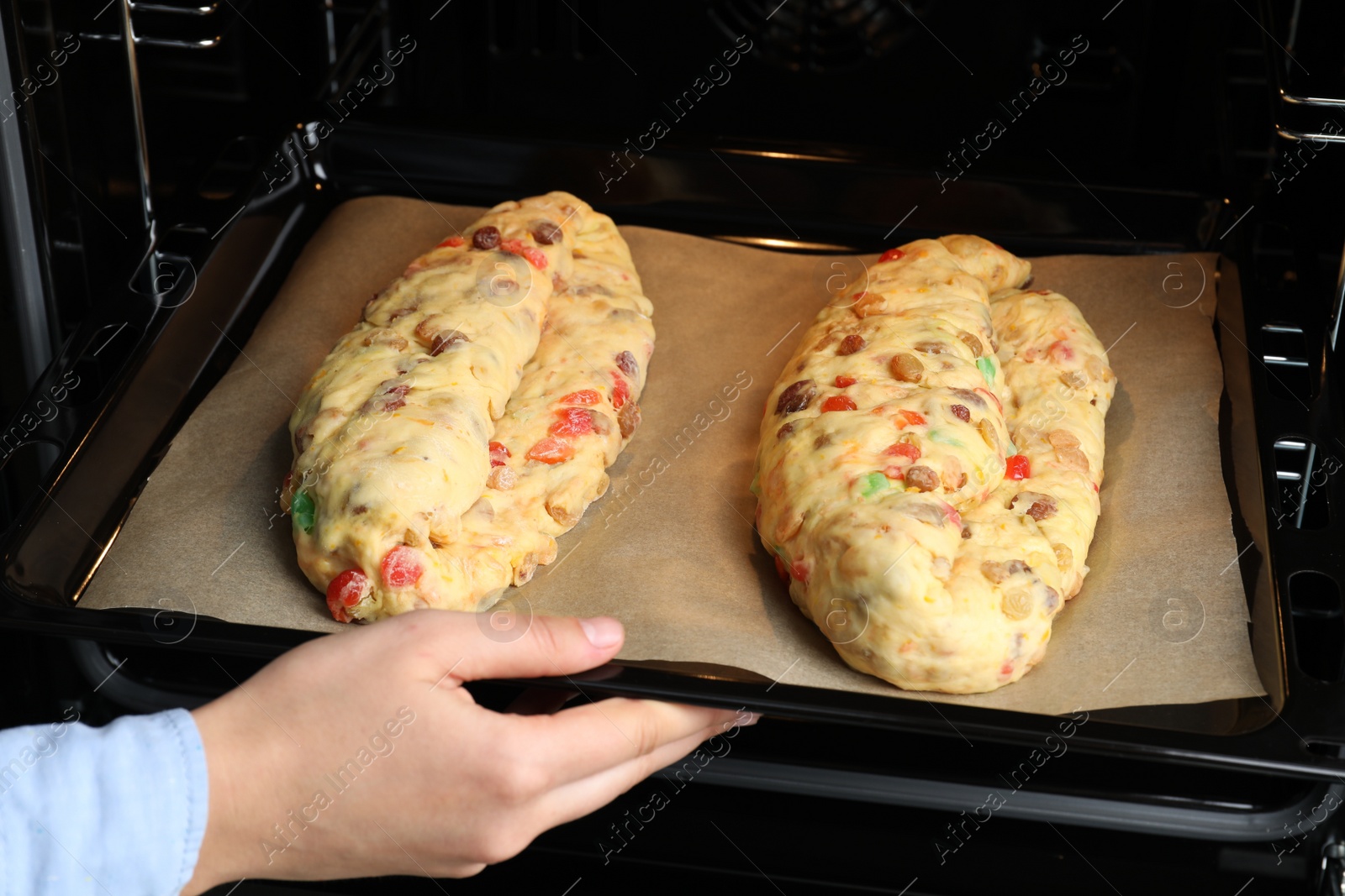 Photo of Woman putting baking tray with raw homemade Stollens into oven, closeup. Traditional German Christmas bread