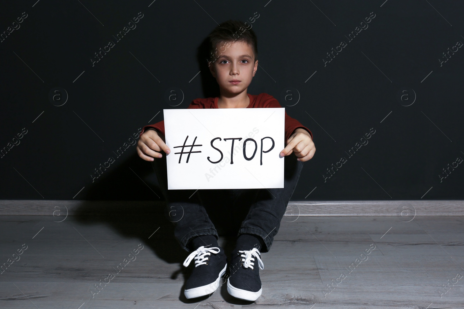 Photo of Abused little boy with hashtag STOP near black wall. Domestic violence concept