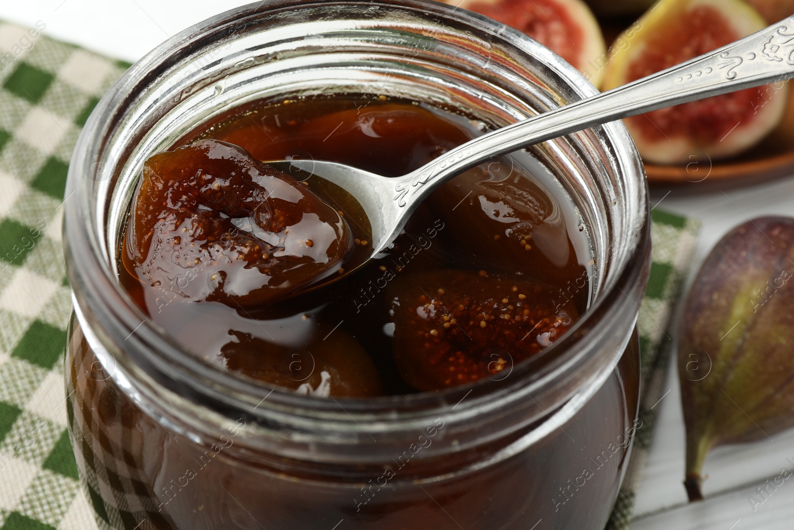 Photo of Jar of tasty sweet fig jam on white table, closeup