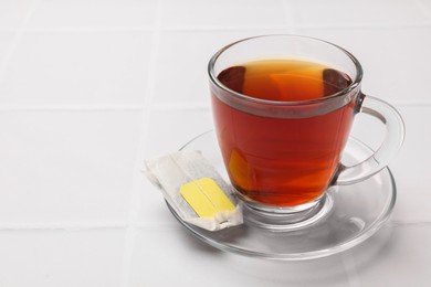 Photo of Tea bag and cup of aromatic drink on white tiled table, closeup. Space for text