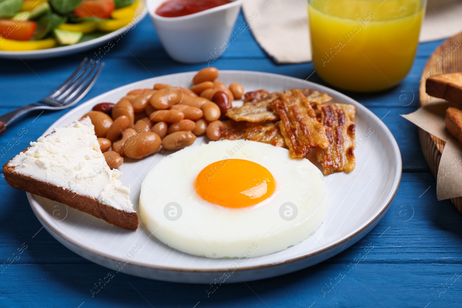 Photo of Tasty breakfast with fried egg, sandwich and bacon served on blue wooden table, closeup