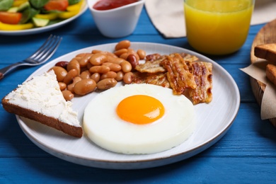 Tasty breakfast with fried egg, sandwich and bacon served on blue wooden table, closeup