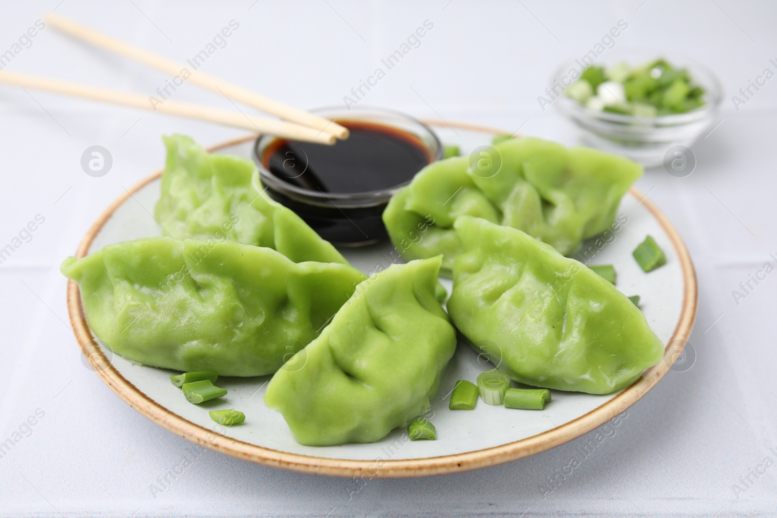Photo of Delicious green dumplings (gyozas) with soy sauce served on white tiled table, closeup