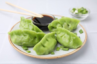 Delicious green dumplings (gyozas) with soy sauce served on white tiled table, closeup