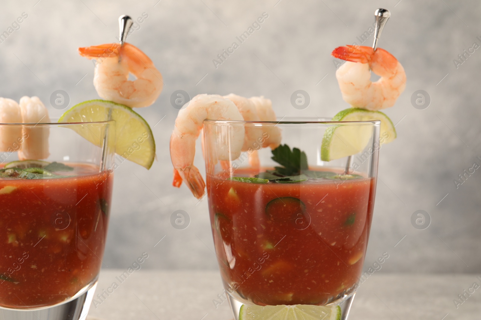 Photo of Tasty shrimp cocktail with sauce in glasses and lime on light table, closeup