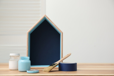 Photo of House shaped shelf, jars of paints and decorator tools on table. Space for text