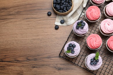 Photo of Sweet cupcakes with fresh blueberries on wooden table, flat lay. Space for text