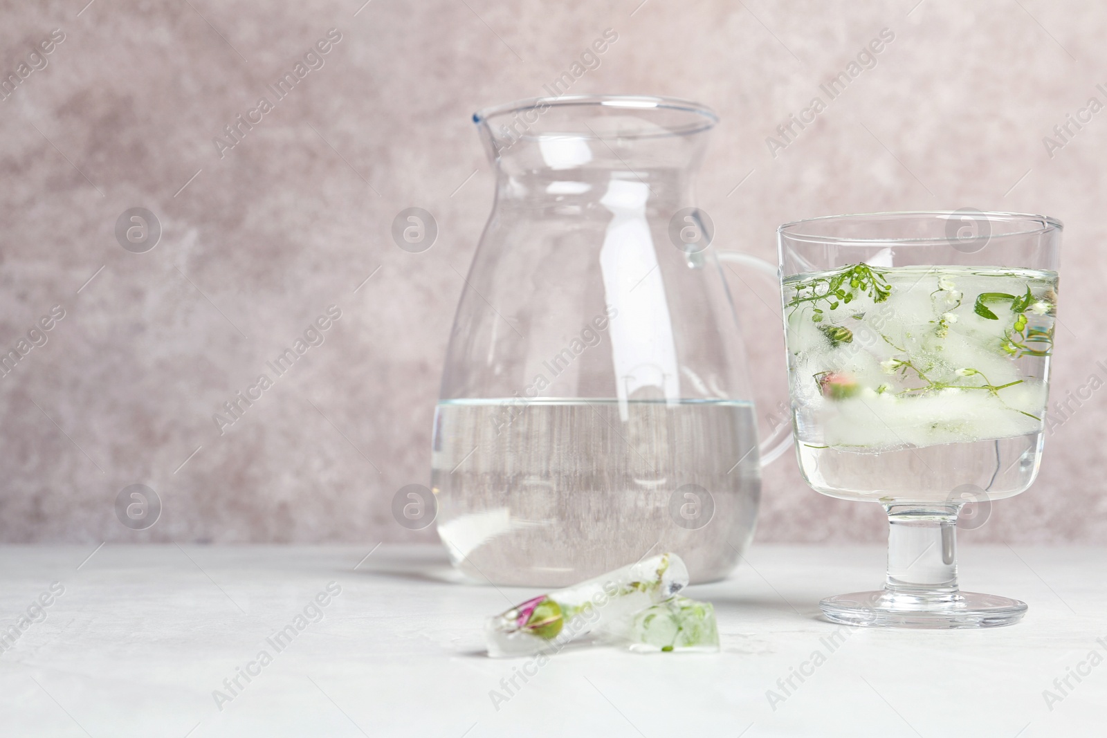 Photo of Glass with floral ice cubes and water near jug on table. Space for text