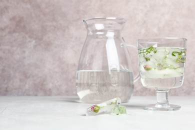 Glass with floral ice cubes and water near jug on table. Space for text