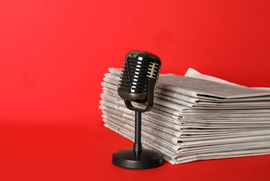 Photo of Newspapers and vintage microphone on red background, space for text. Journalist's work