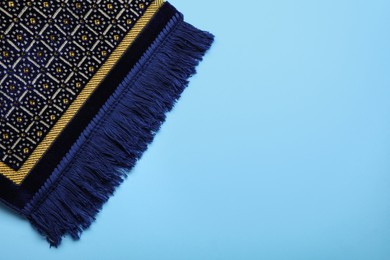 Photo of Muslim prayer rug on light blue background, top view. Space for text