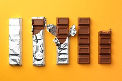 Photo of Tasty chocolate bars on yellow background, flat lay