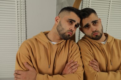 Sad young man near mirror at home