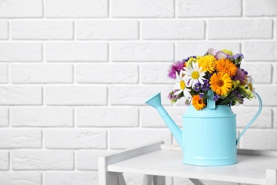 Photo of Watering can with beautiful wild flowers on table near brick wall